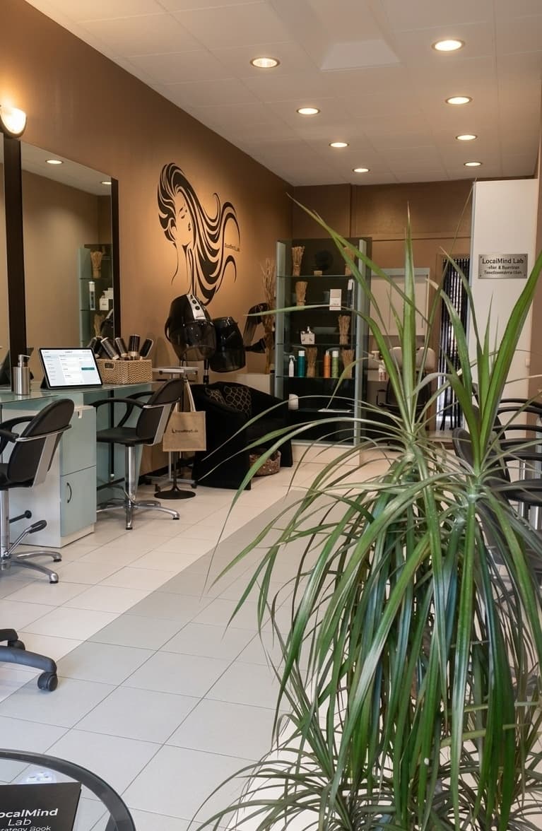 Salone di bellezza moderno con postazioni eleganti, specchi, decorazione murale e una grande pianta verde.